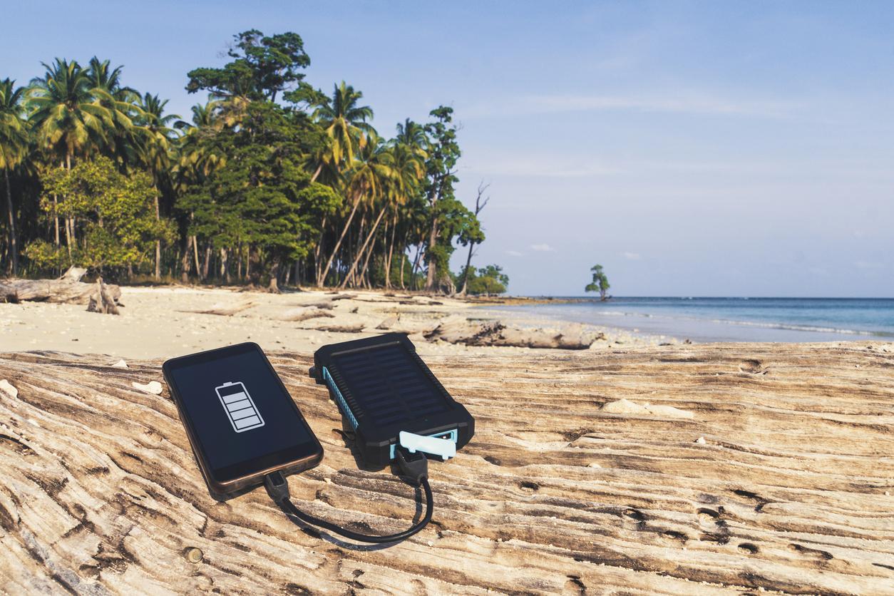 Solar battery and phone lying on rock at the beach